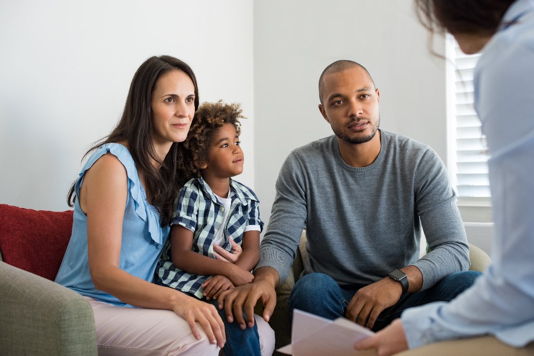 Woman holding her son seated next to her husband listening to someone who is seated across from them