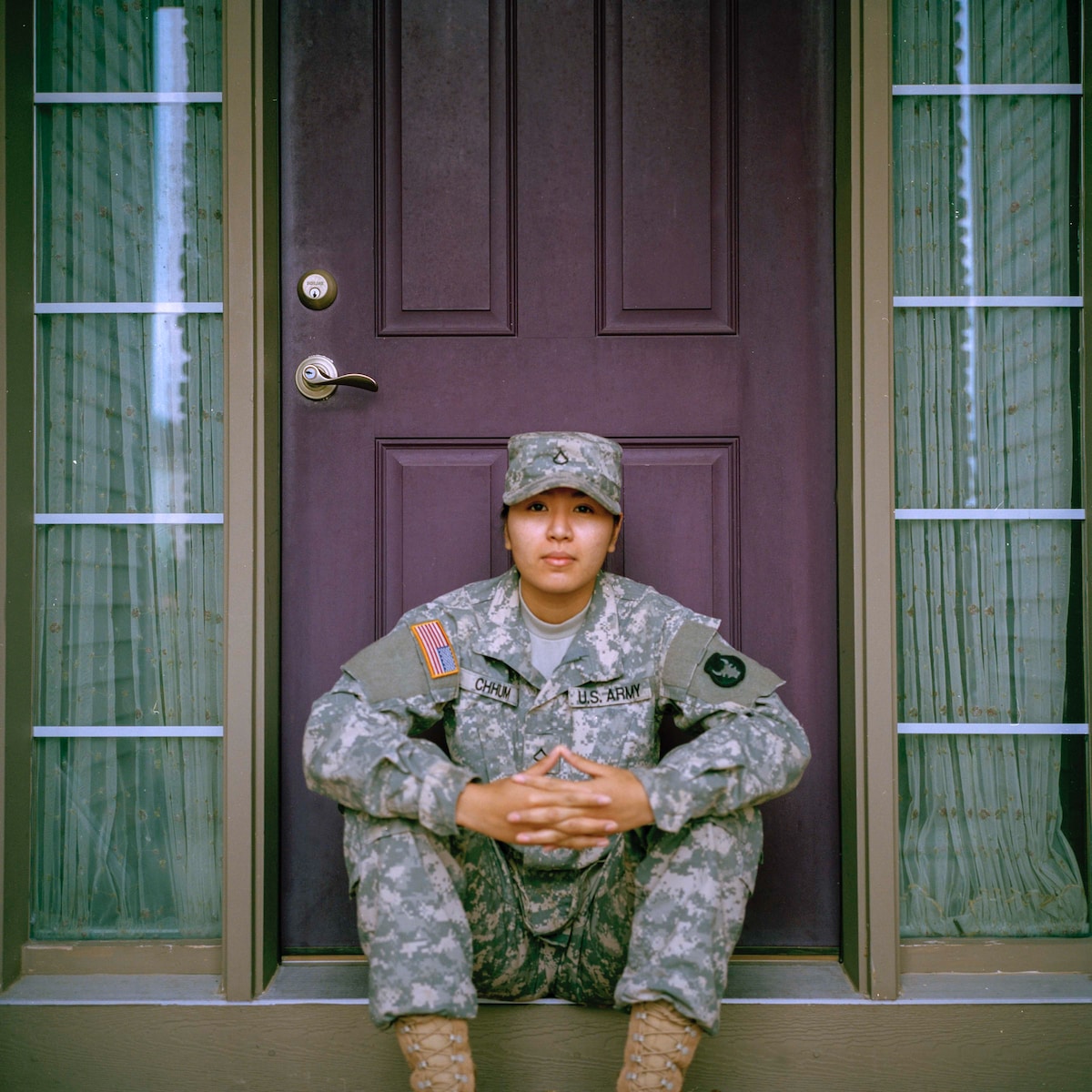 woman in an Army field uniform sitting in front of closed door