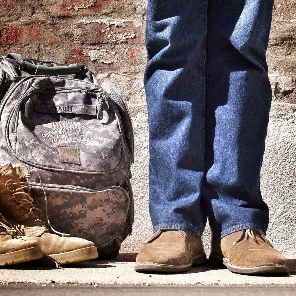A person in normal attire with a military backpack and boots to the side meant to indicate the person is transitioning for military to civilian life.