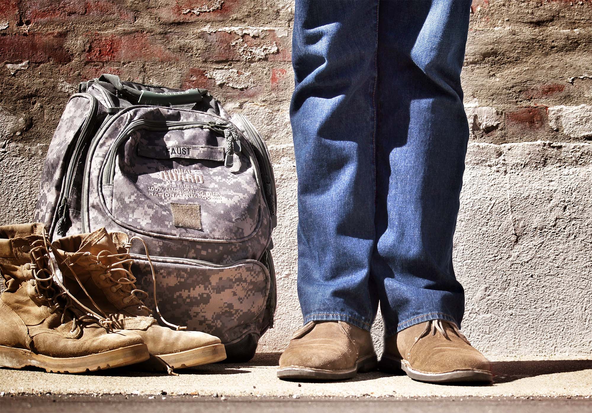 A person in normal attire with a military backpack and boots to the side meant to indicate the person is transitioning for military to civilian life.